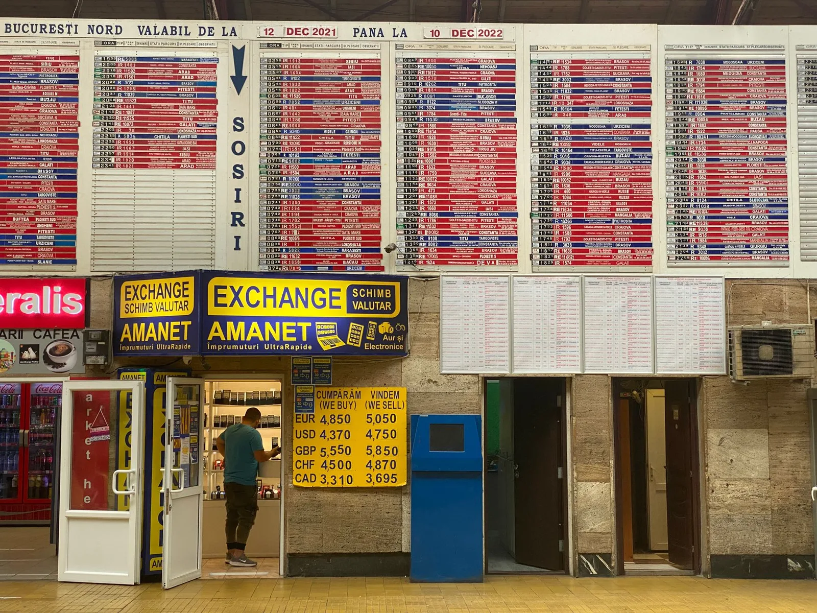 דוכן חלפן כספים מורשה בבאלי עם שלט ומחירון שערים גלוי, ספירת שטרות רופיה בשקיפות מול הלקוח
